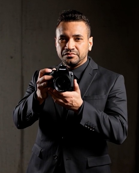Vinicius Lima segurando uma câmera fotográfica, de terno preto